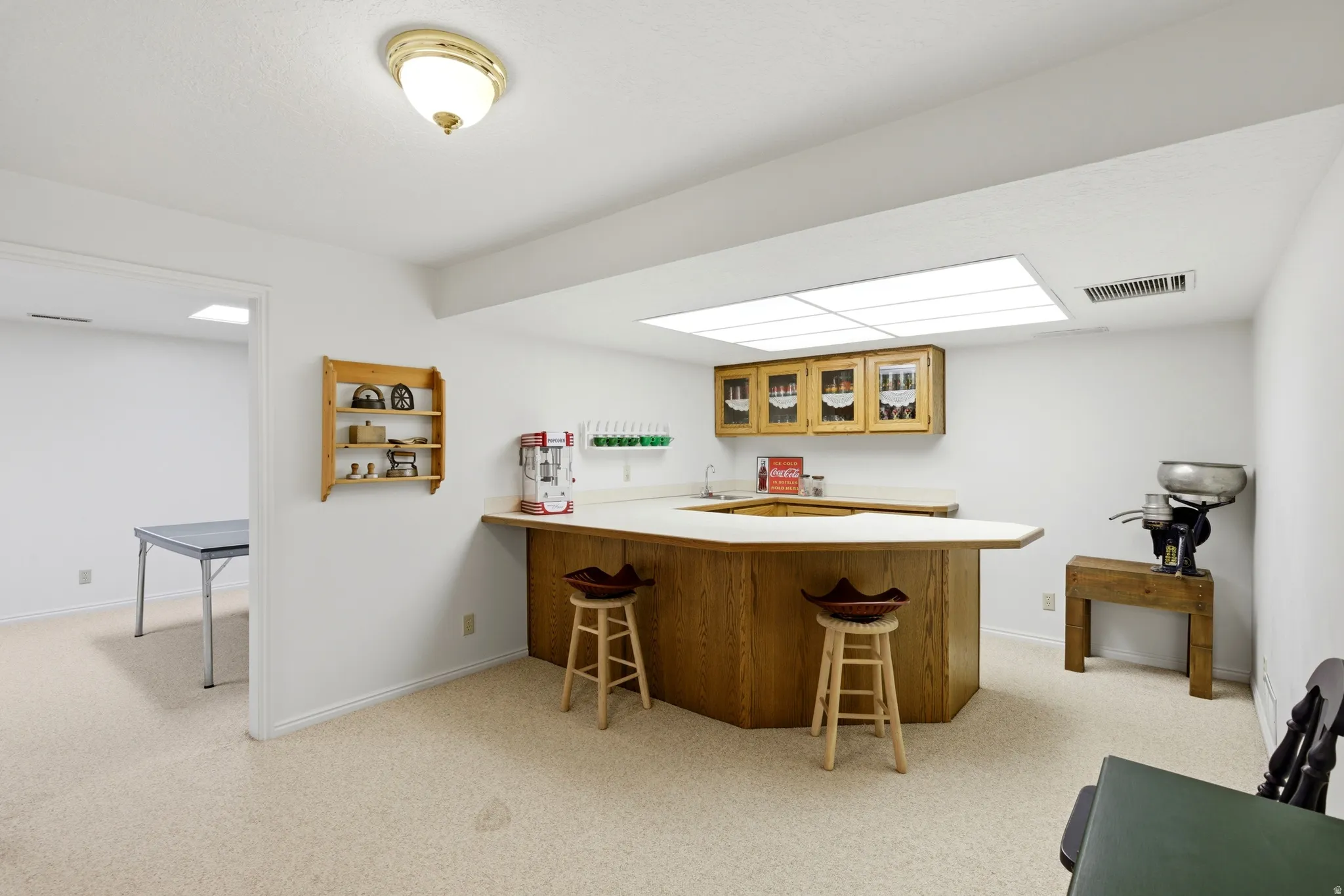 Indoor wet bar featuring light countertops, wood finish cabinets, light colored carpet, and glass fronted cabinets