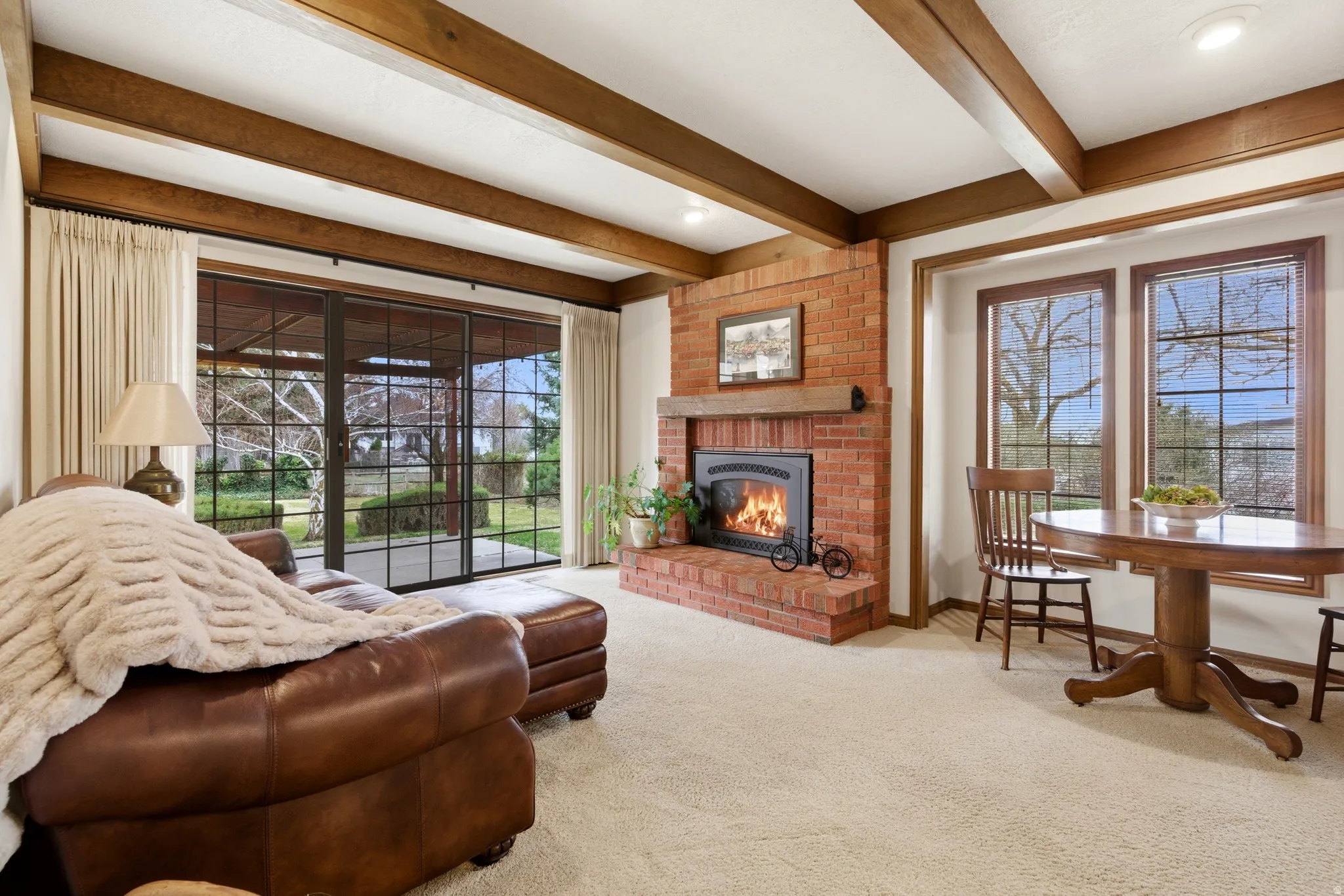 Living room with carpet flooring, a brick fireplace, healthy amount of natural light, and beam ceiling