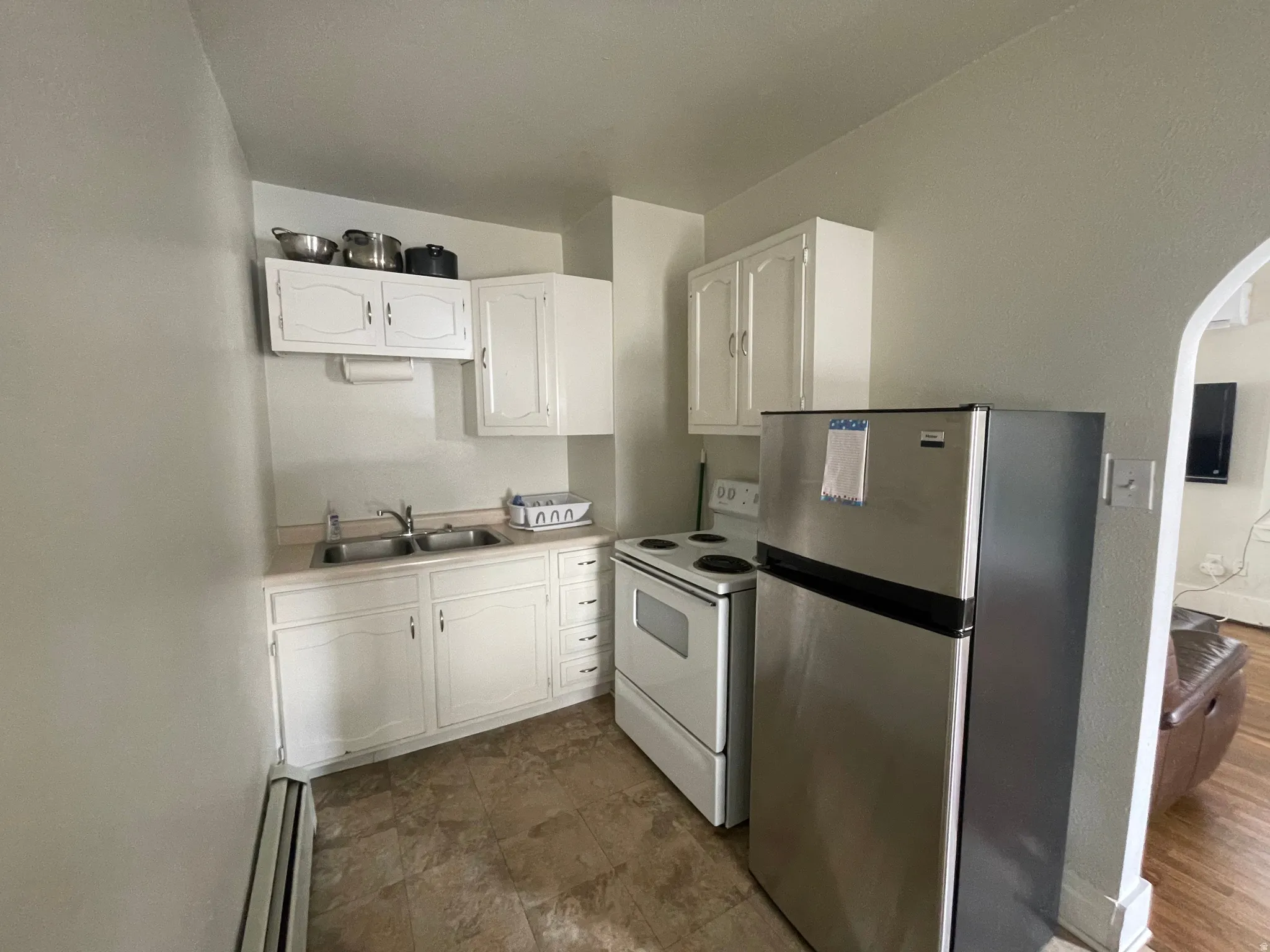 Kitchen featuring white cabinets, freestanding refrigerator, a baseboard radiator, electric range, and arched walkways