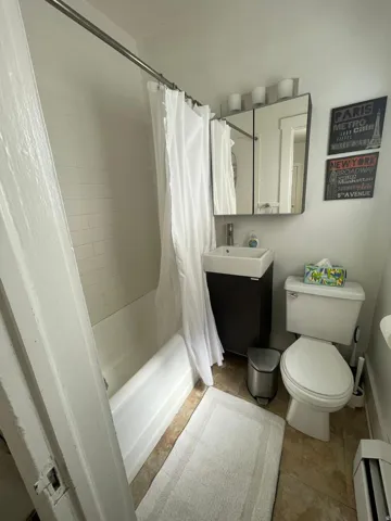 Full bath featuring vanity, shower / bath combination with curtain, light tile patterned floors, and a baseboard radiator
