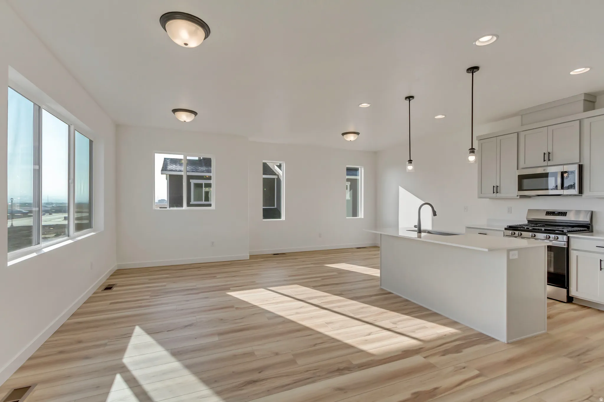Kitchen featuring stainless steel appliances, a kitchen island with sink, light wood-type flooring, decorative light fixtures, and plenty of natural light