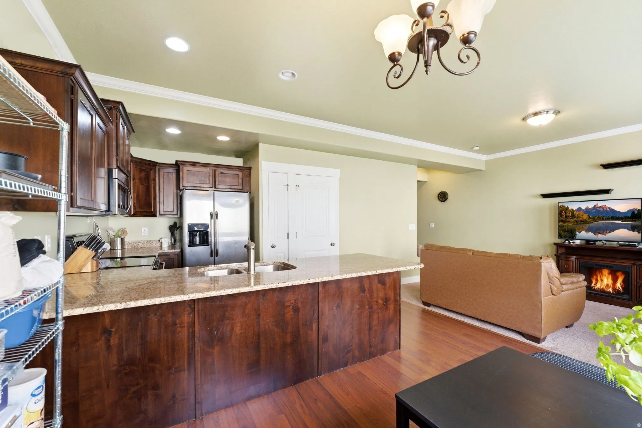 Kitchen featuring dark wood cabinetry, crown molding, stainless steel appliances, accented with light granite counters