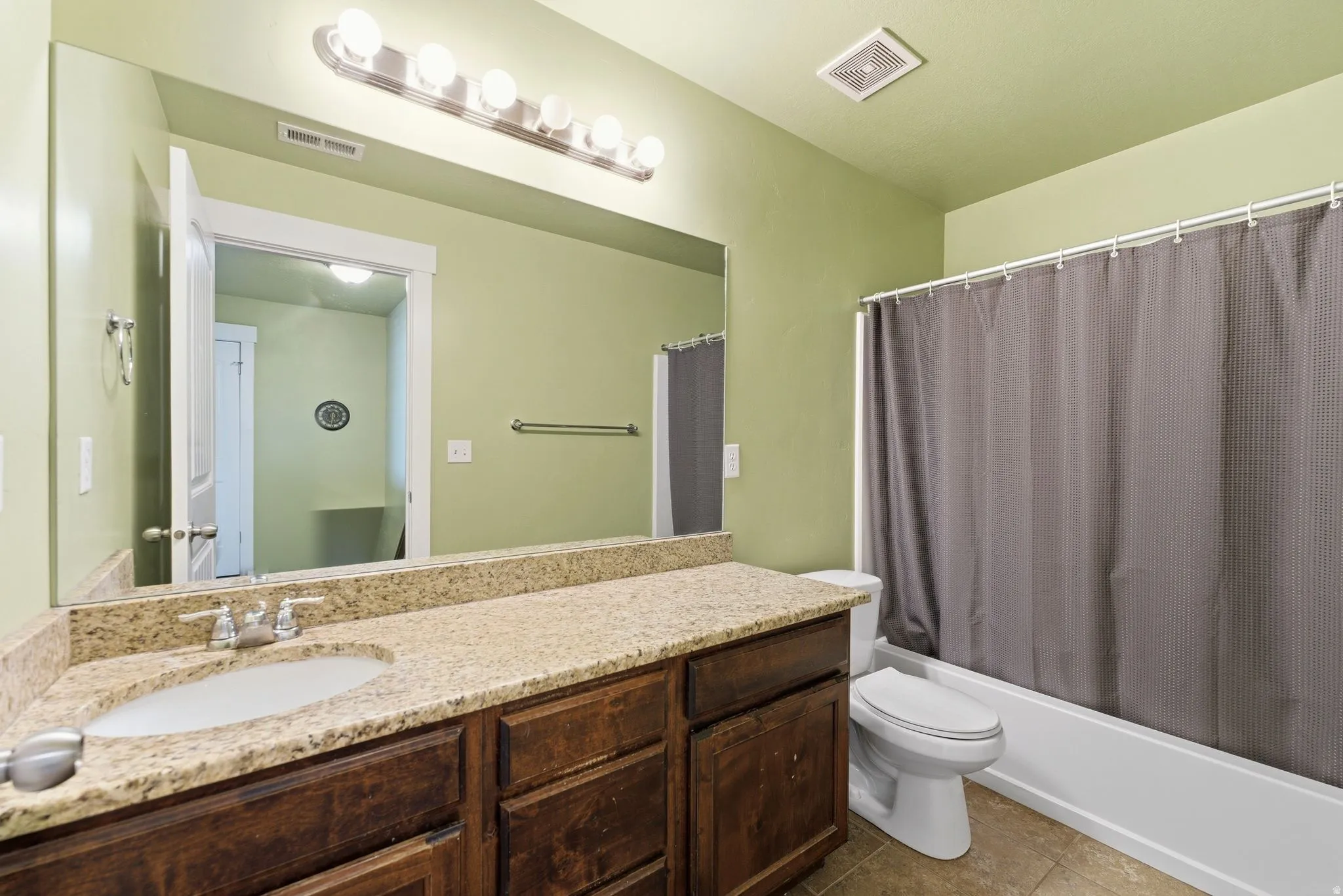 Bathroom featuring oversized vanity with dark cabinetry and light granite counters, shower / tub