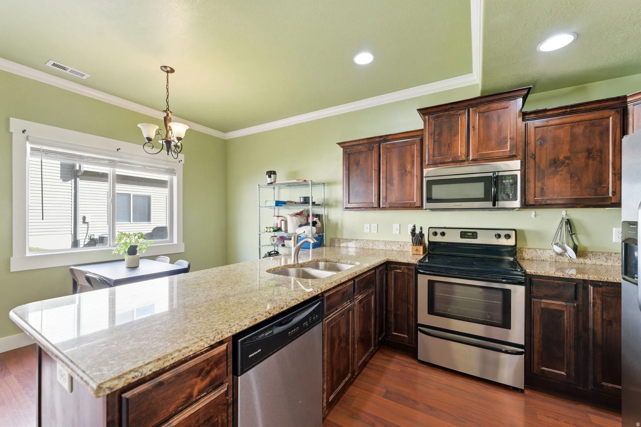 Kitchen featuring stainless steel appliances, a peninsula, light granite counters, dark wood laminate, and ornamental molding
