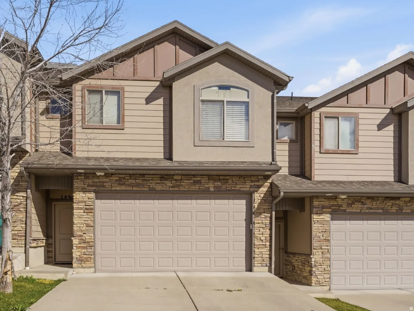 View of front of house with board and batten siding, stone siding, an attached garage, and concrete driveway.