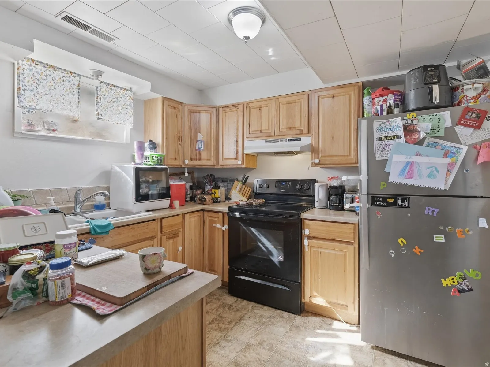 Kitchen with freestanding refrigerator, black range with electric stovetop, light countertops, light wood finish cabinets, and white microwave