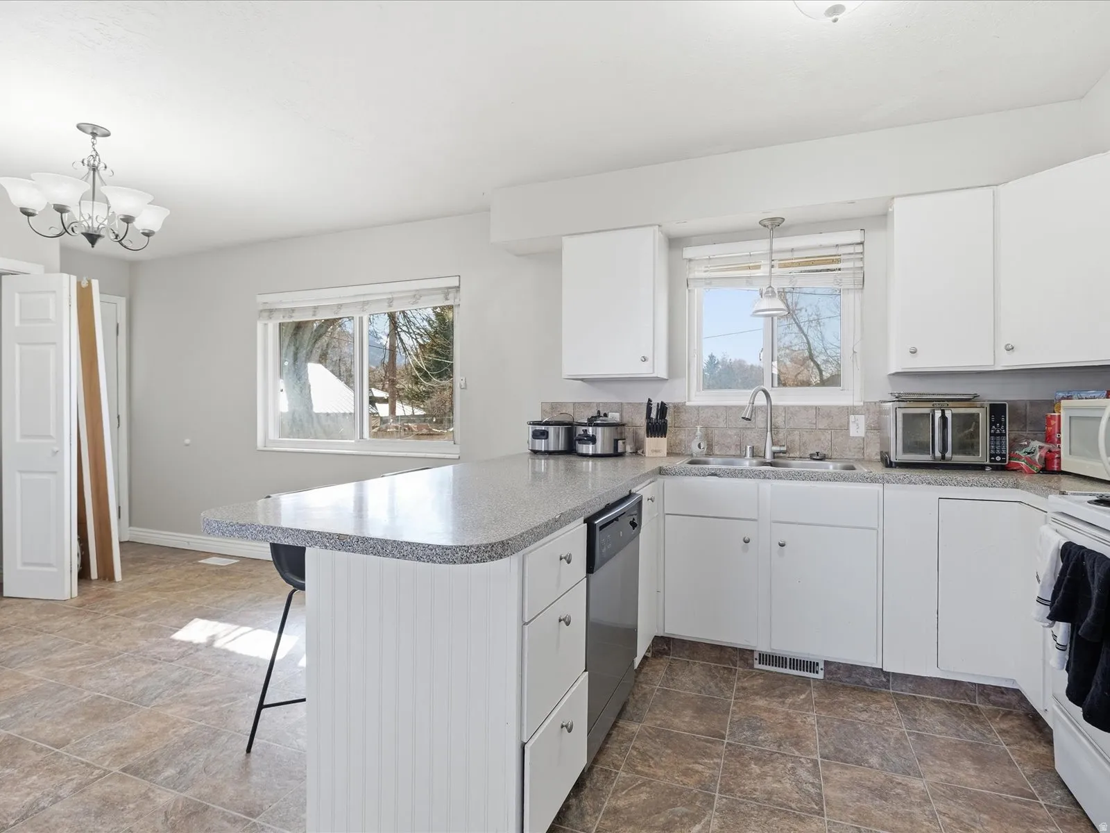 Kitchen with white cabinetry, stone finish floors, a kitchen bar, a peninsula, and light countertops