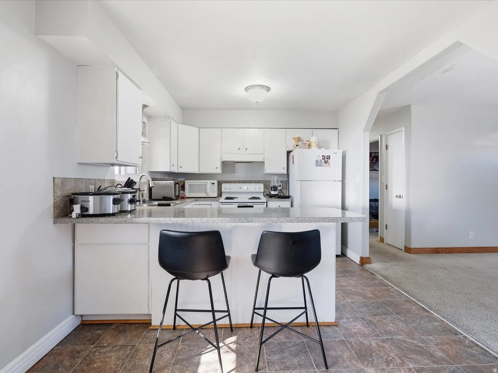 Kitchen featuring light countertops, white cabinets, a peninsula, white appliances, and stone finish floors