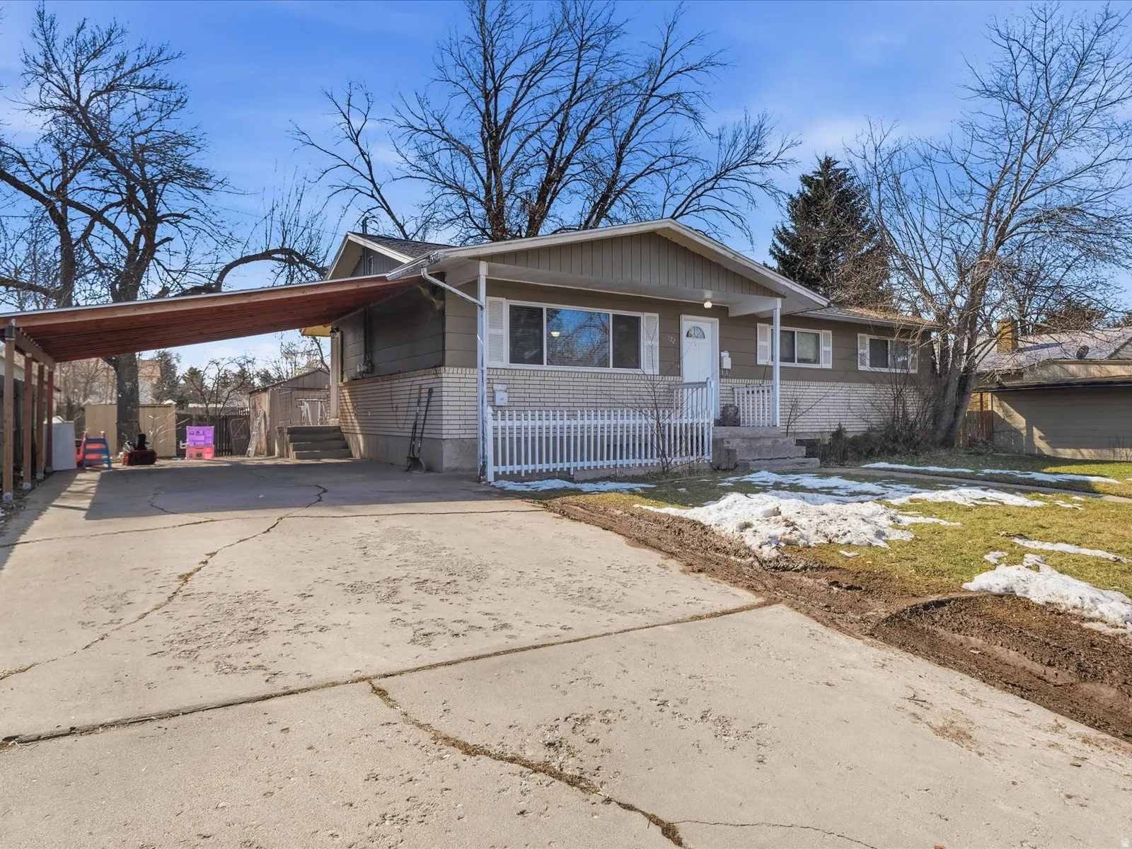 View of front of house with concrete driveway, a carport, covered porch, and brick siding