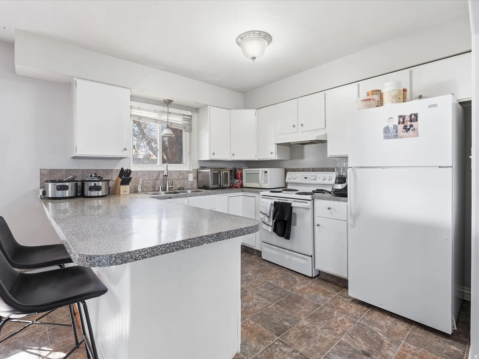 Kitchen featuring white appliances, a breakfast bar area, a peninsula, white cabinets, and stone finish floors