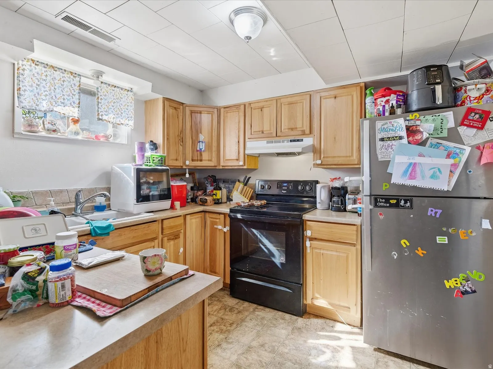 Kitchen featuring freestanding refrigerator, light countertops, black electric range oven, and light wood finish cabinetry