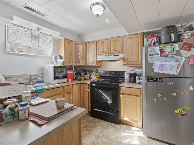 Kitchen with freestanding refrigerator, black range with electric stovetop, light countertops, light wood finish cabinets, and white microwave