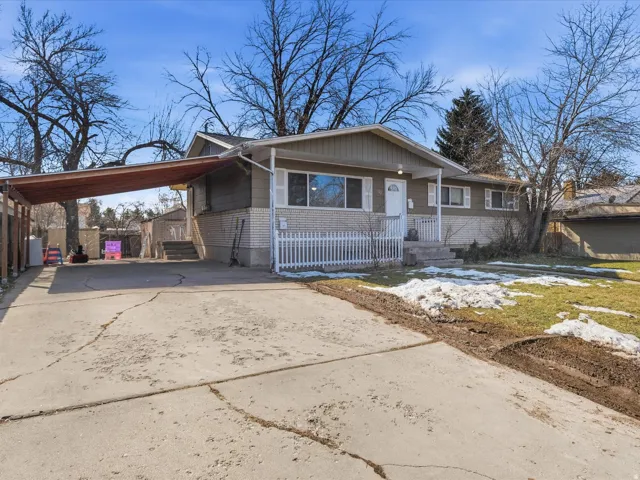 View of front of house with concrete driveway, a carport, covered porch, and brick siding