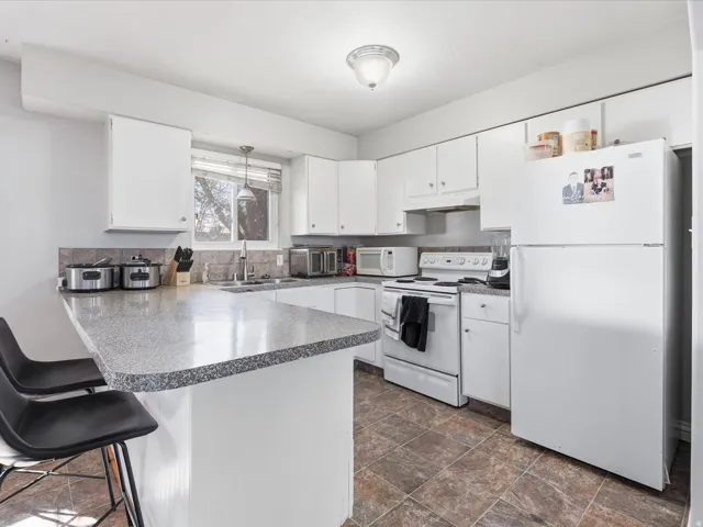 Kitchen featuring white appliances, a breakfast bar area, a peninsula, white cabinets, and stone finish floors