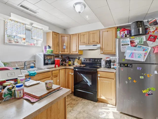 Kitchen featuring freestanding refrigerator, light countertops, black electric range oven, and light wood finish cabinetry