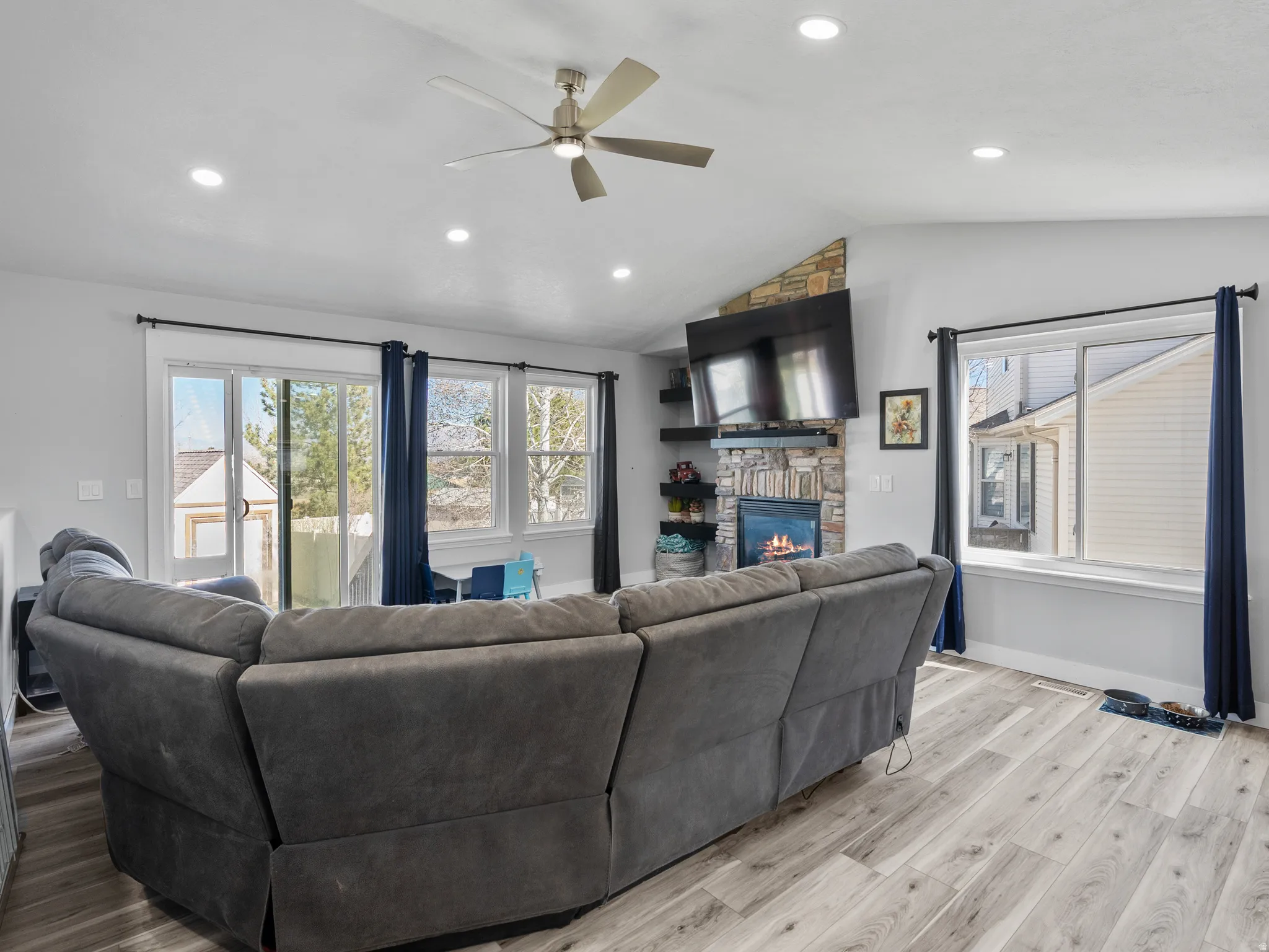 Living room featuring light wood-type flooring, ceiling fan, a large fireplace, and recessed lighting