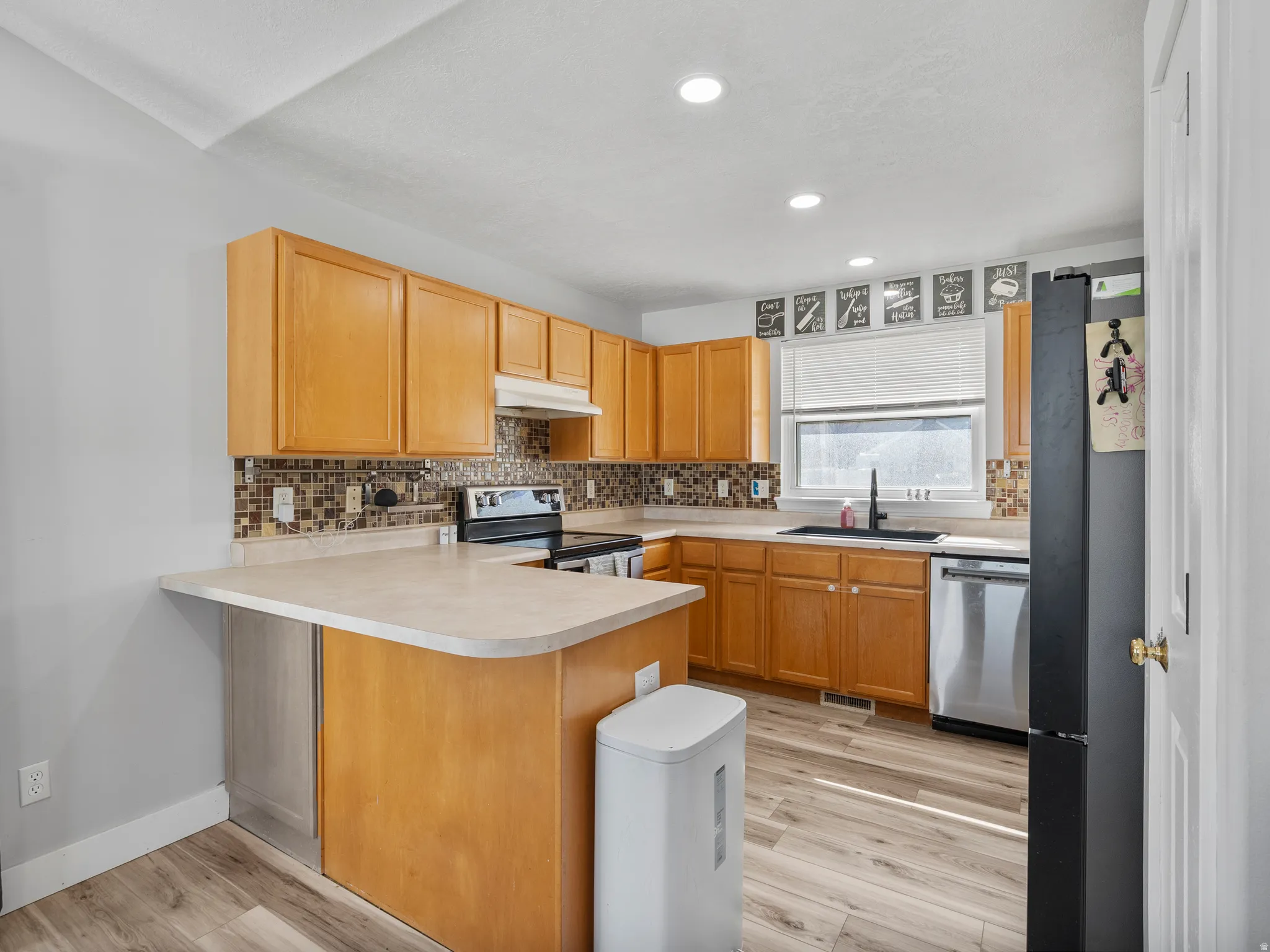 Kitchen featuring a peninsula, light countertops, stainless steel appliances, light wood-style floors, and recessed lighting