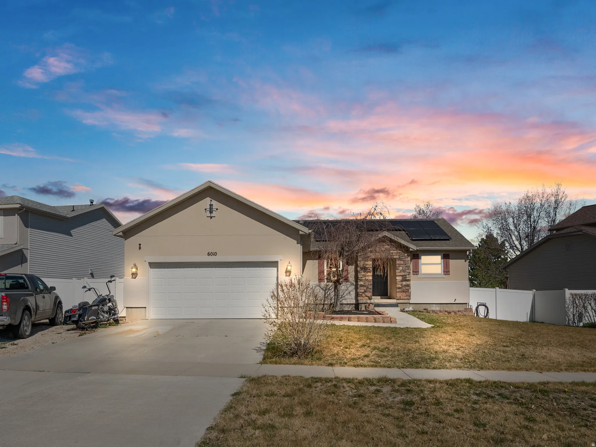 Ranch-style house with roof mounted solar panels, a garage, concrete driveway, stone siding, and stucco siding