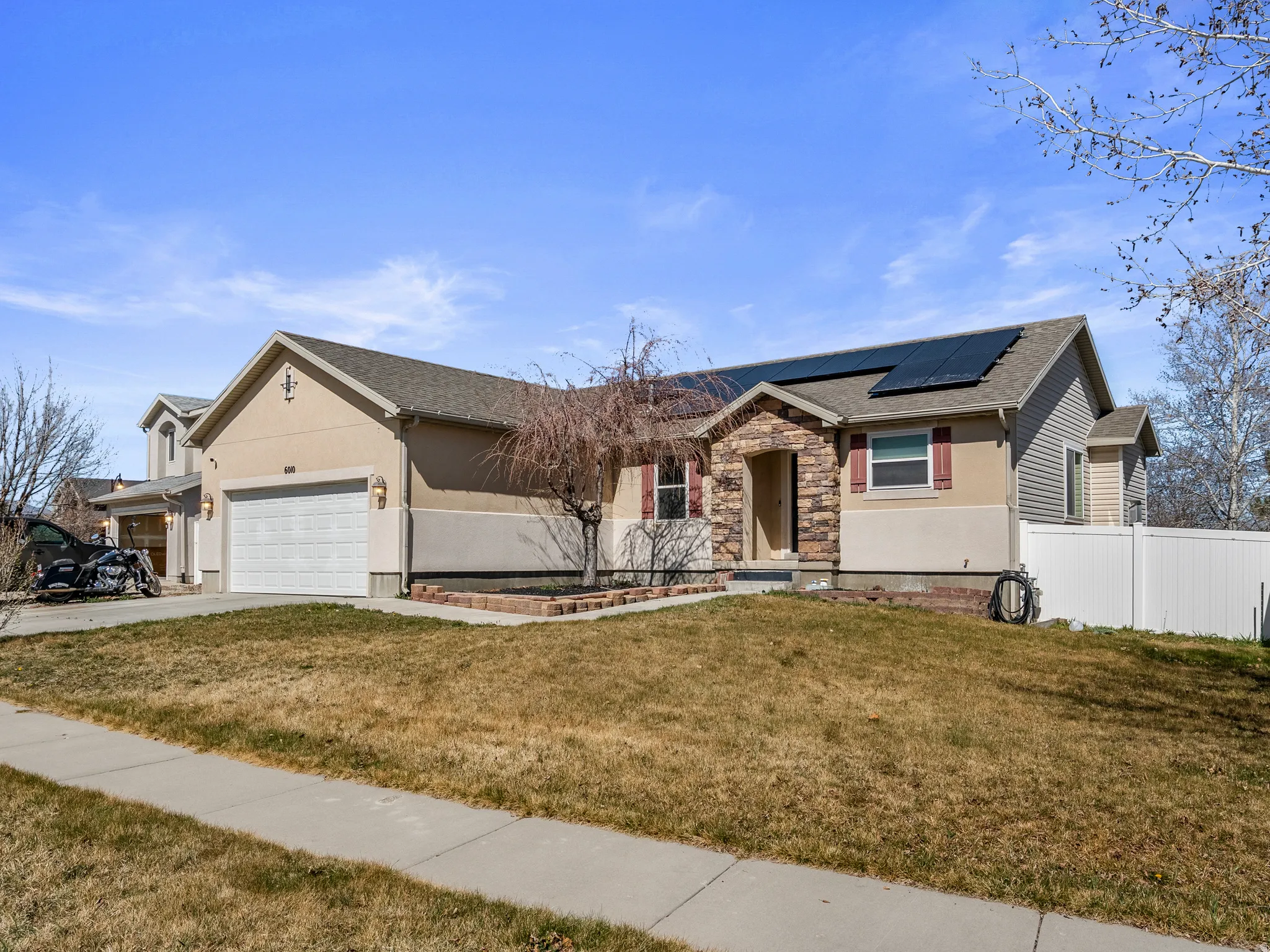 Ranch-style home with stone siding, roof mounted solar panels, an attached garage, and stucco siding