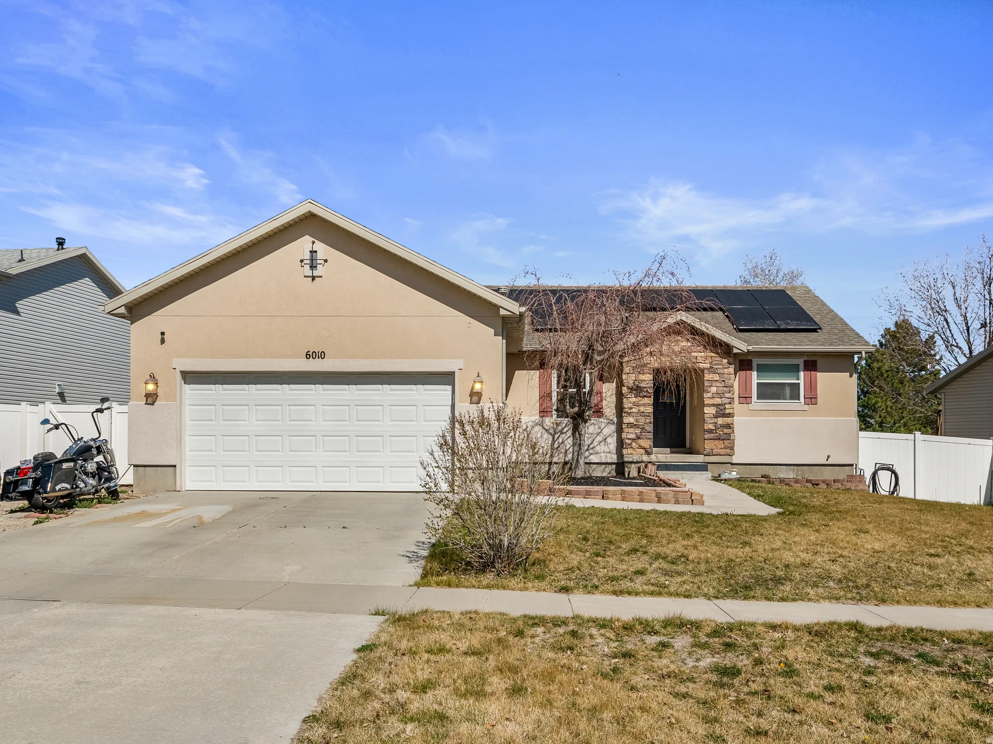 Ranch-style home featuring roof mounted solar panels, concrete driveway, a garage, and stucco siding
