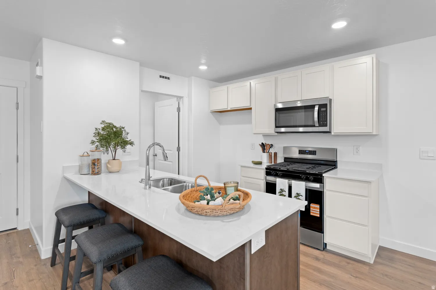 Kitchen with a breakfast bar, stainless steel appliances, a peninsula, light stone counters, and light wood-style flooring
