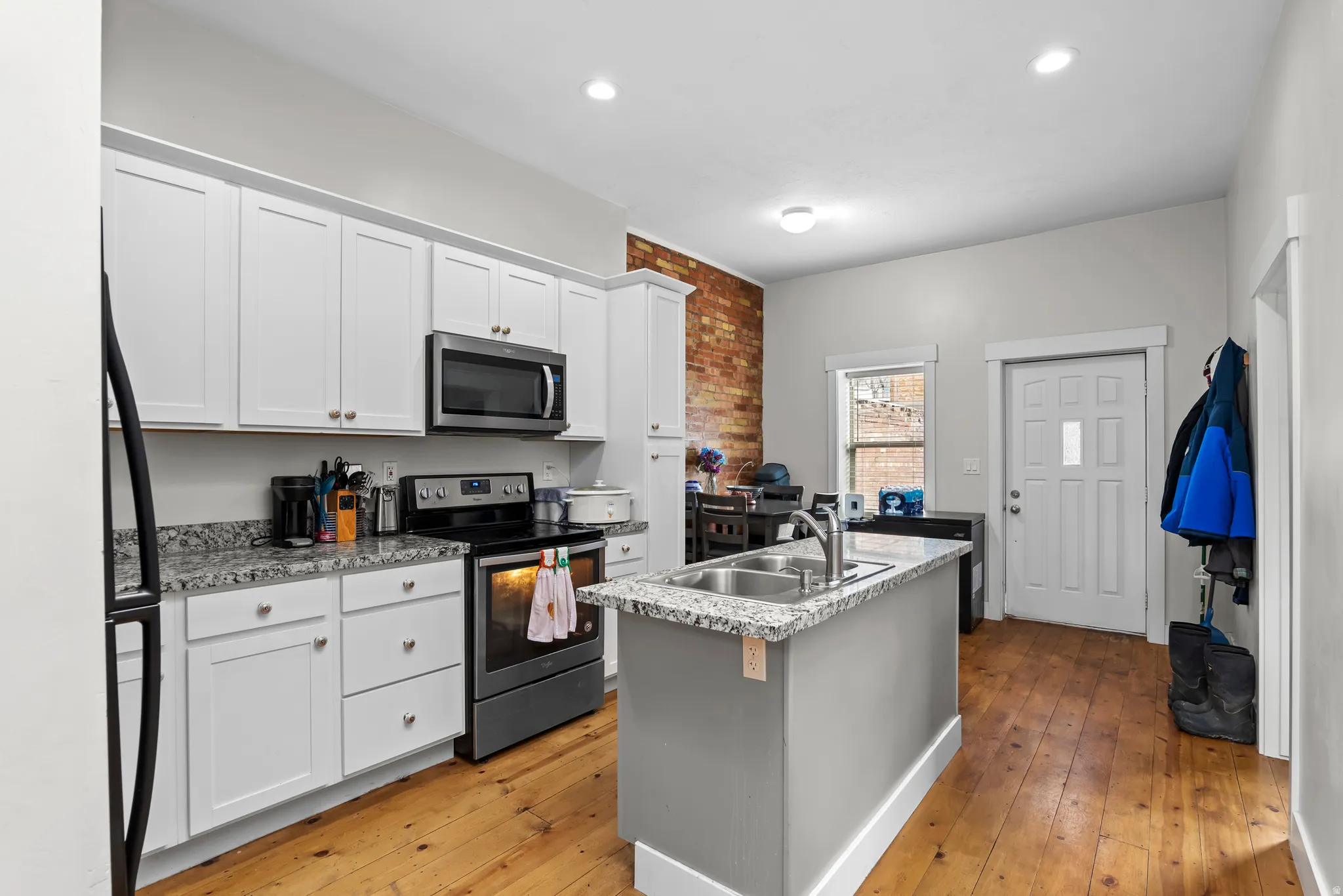 Second level apartment - Kitchen with stainless steel appliances, a center island with sink, light wood-type flooring, white cabinets, and brick wall
