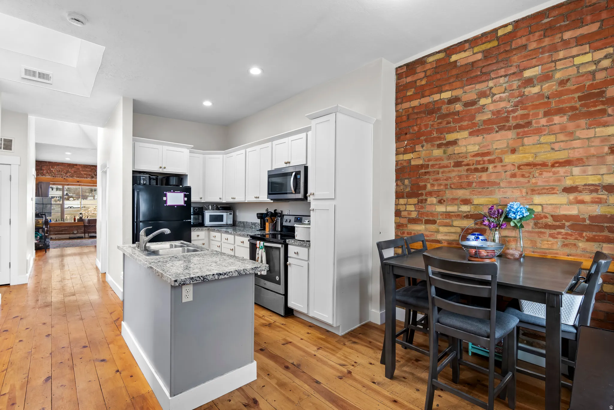 Send level apartment - Kitchen with brick wall, stainless steel appliances, light wood finished floors, white cabinets, and a center island with sink
