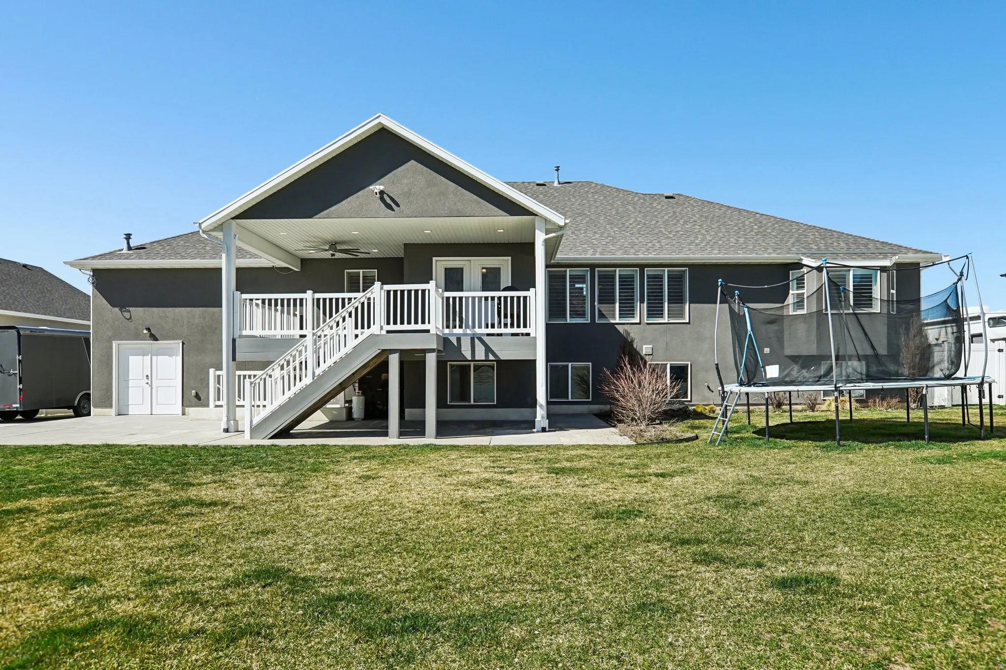 Rear view of house with a patio area, a ceiling fan, a yard, and a trampoline