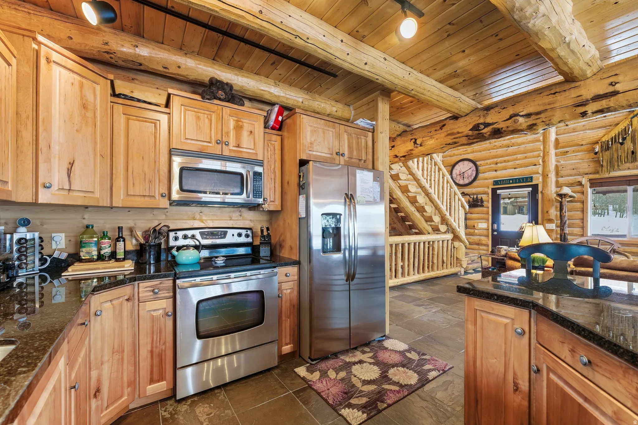 Kitchen featuring log walls, stainless steel appliances, a wood ceiling with exposed beams, dark stone countertops, and wood finish cabinetry