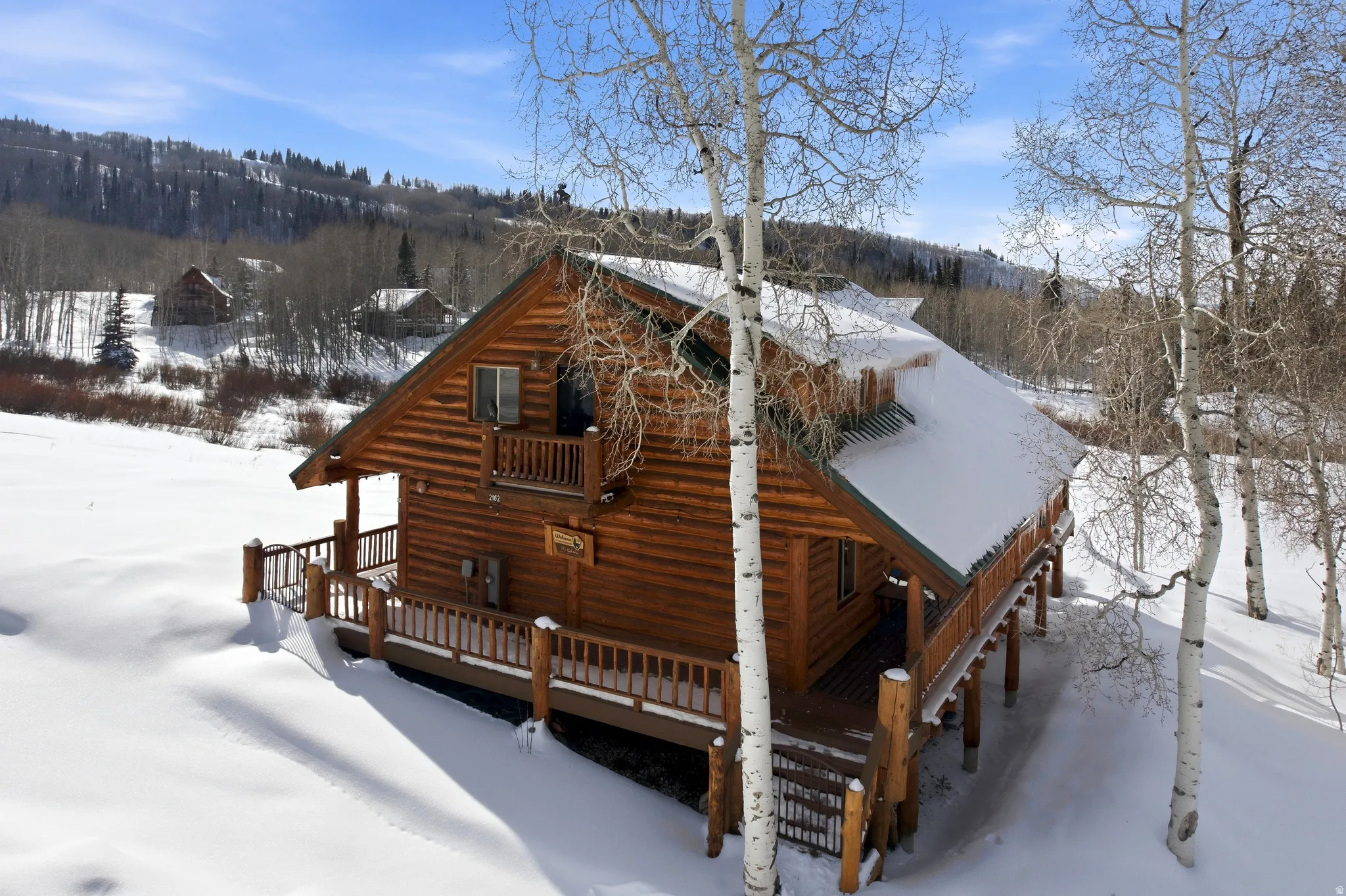 View of snow covered exterior featuring a deck and a wooded view