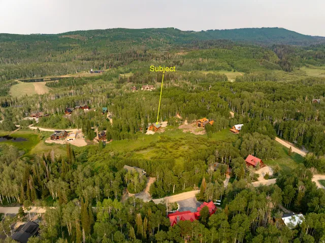 Mountainous landscape with expansive tree coverage and scattered residential properties, featuring a subject property surrounded by dense forest