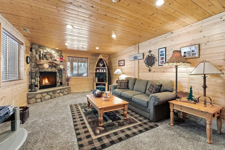 Living area with wood walls, recessed lighting, carpet floors, a stone fireplace, and wooden ceiling