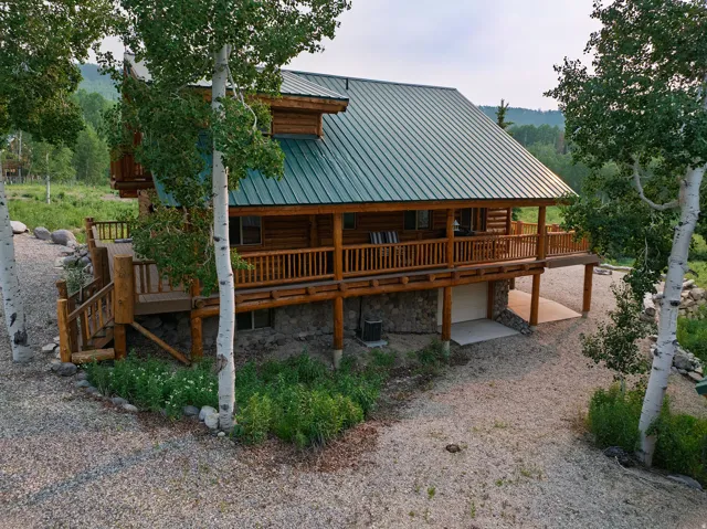 Log cabin exterior featuring a green metal roof, extensive wrap-around deck, and a stone foundation