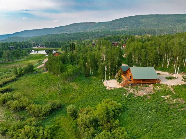 Log cabin style property featuring a green metal roof, a wrap-around porch, and a gravel driveway