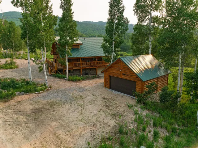 Log cabin style home featuring a covered deck, green metal roofing, and natural wood siding