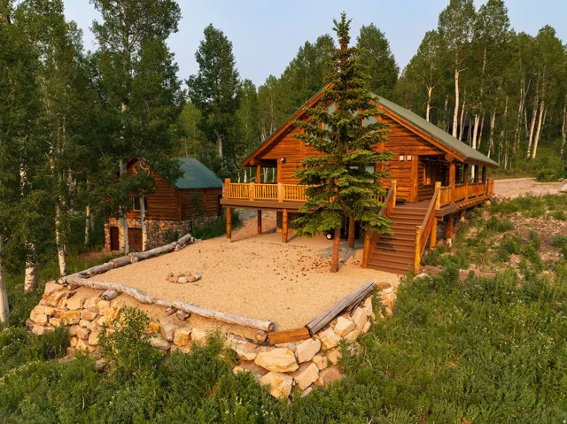 Log home exterior with a covered porch and extended wood deck featuring a balustrade railing