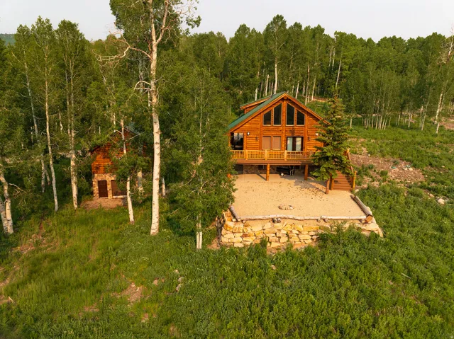 Custom log home featuring a green metal roof, a full-width timber deck, and expansive A-frame windows