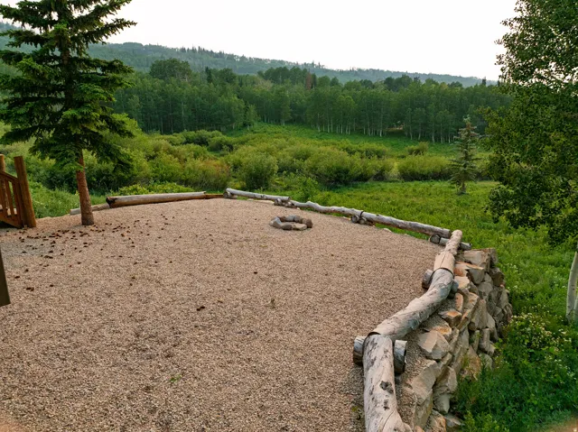 Gravel patio area featuring a built-in fire pit, log-style perimeter, and a stone retaining wall