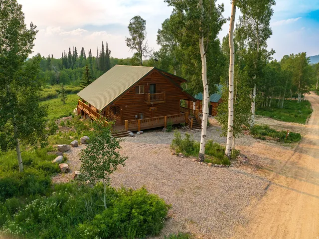 Log cabin exterior featuring a gabled metal roof, expansive decking, and a second-story balcony