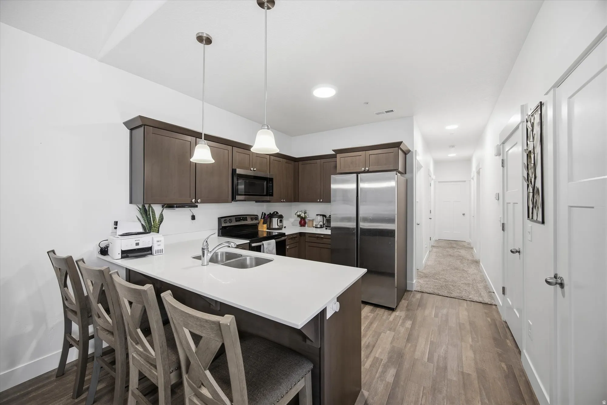 Kitchen featuring dark wood finish cabinets, a kitchen breakfast bar, a peninsula, stainless steel appliances, and light wood-style floors