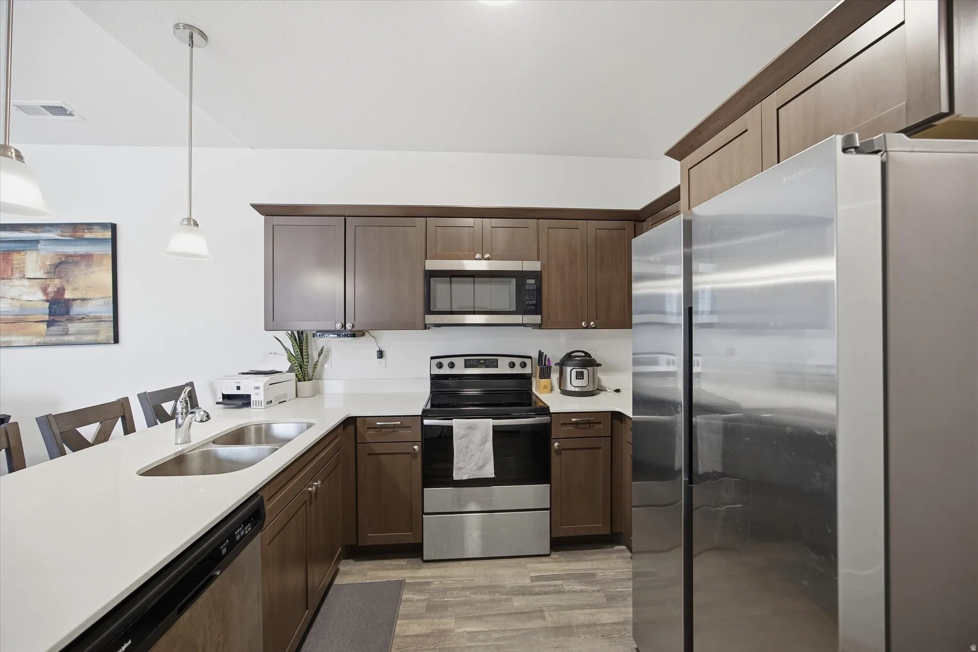 Kitchen featuring stainless steel appliances, a breakfast bar, pendant lighting, a peninsula, and dark wood finish cabinets