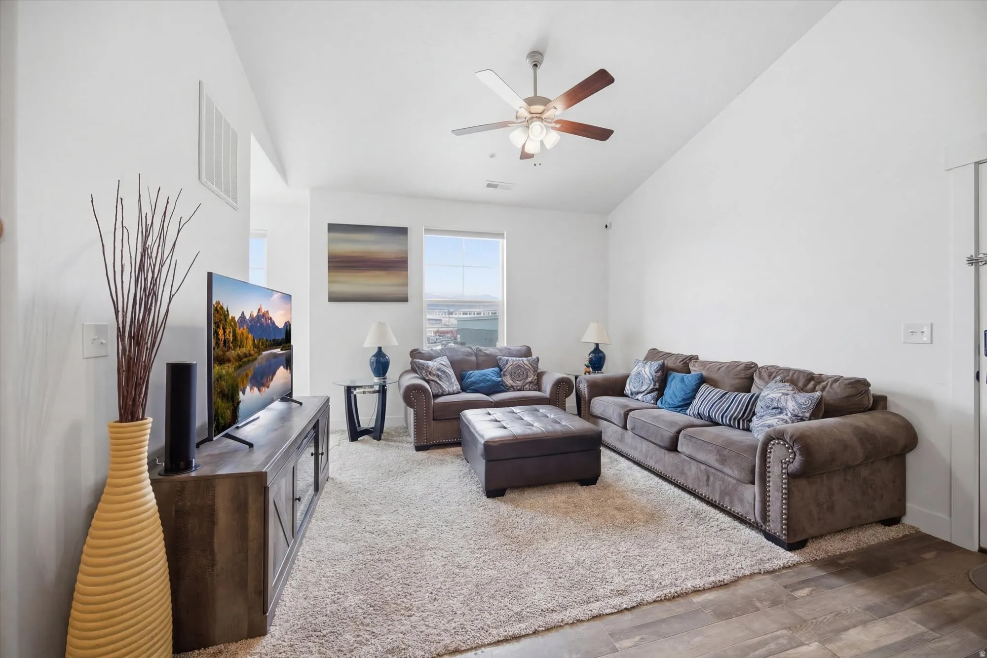 Living area featuring vaulted ceiling, light wood finished floors, and ceiling fan