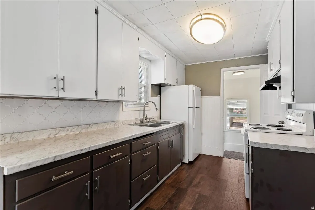 Kitchen with white appliances, light countertops, dual tone cabinets, dark wood-type flooring, and wainscoting