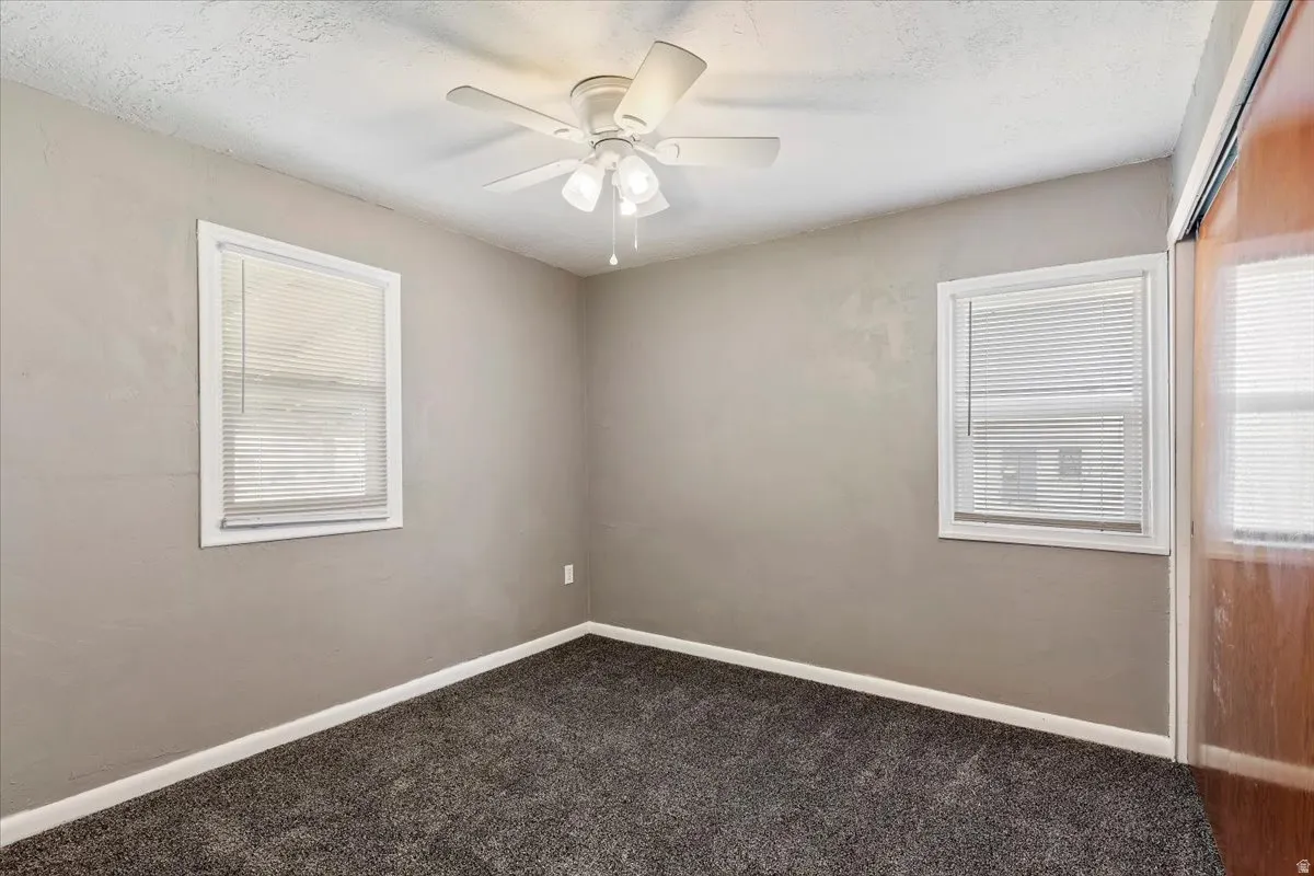 Unfurnished room featuring a ceiling fan and dark colored carpet