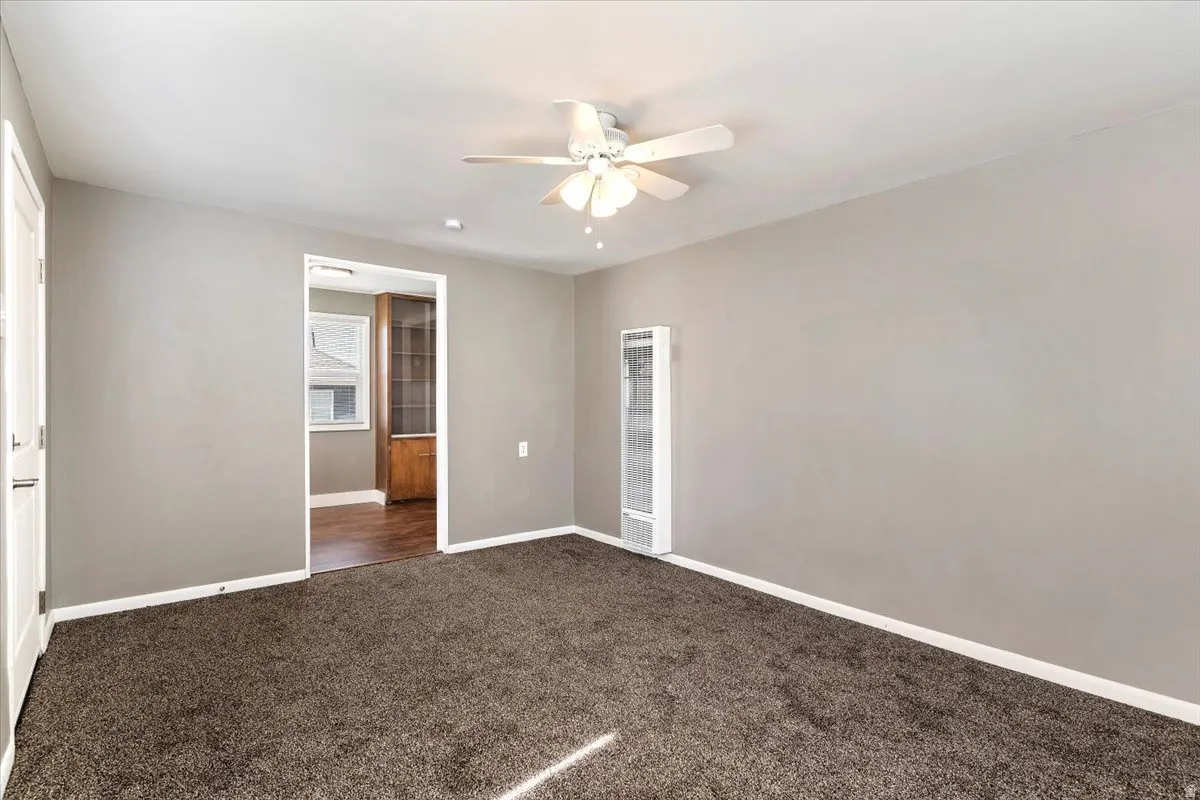 Unfurnished bedroom featuring a heating unit, dark colored carpet, and ceiling fan