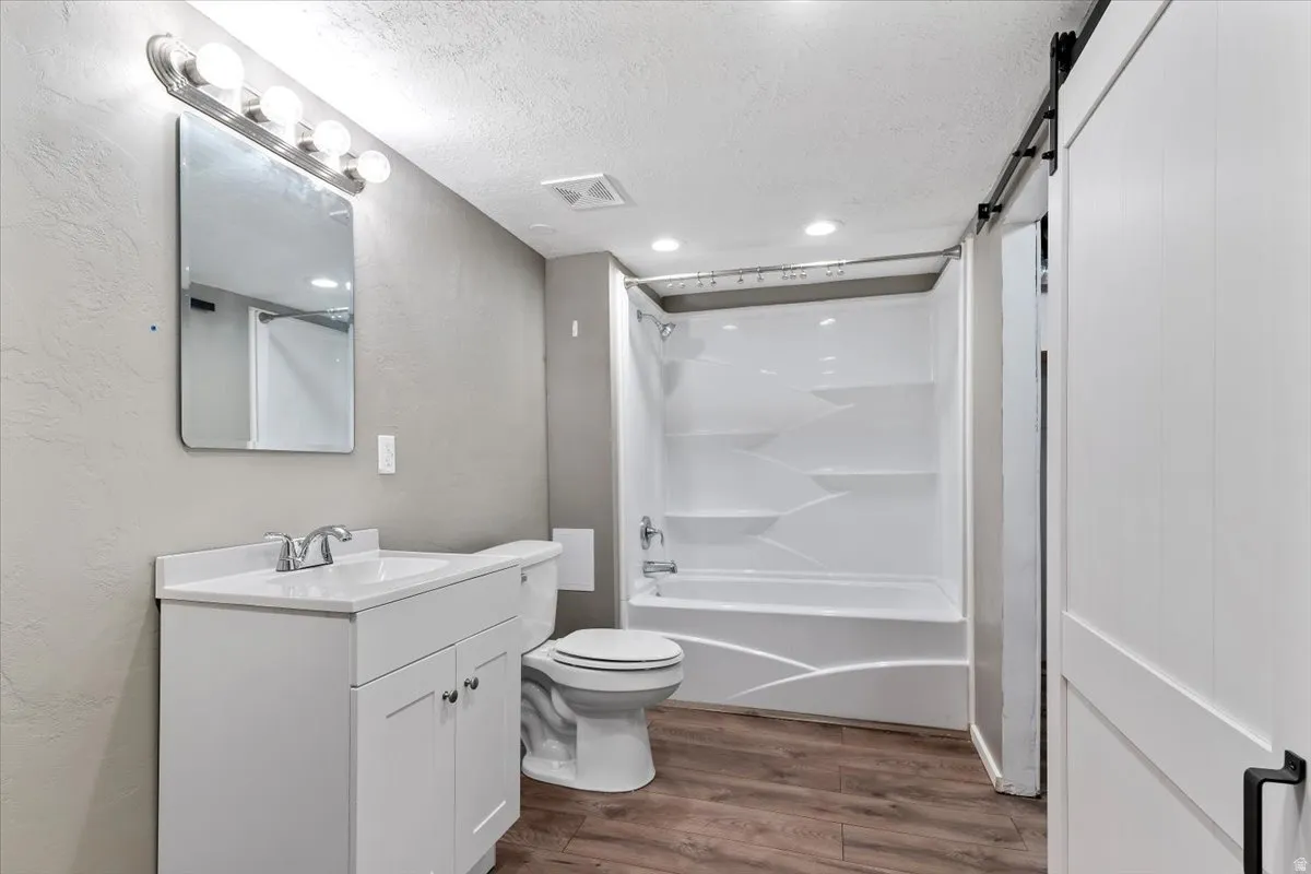 Full bath featuring vanity, a textured ceiling, dark wood finished floors, shower / bath combination, and a textured wall
