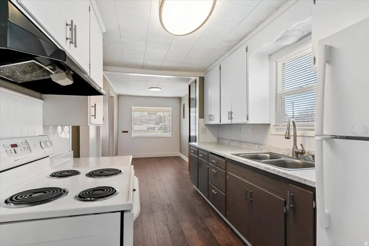 Kitchen with white appliances, two tone cabinetry, light countertops, healthy amount of natural light, and dark wood finished floors