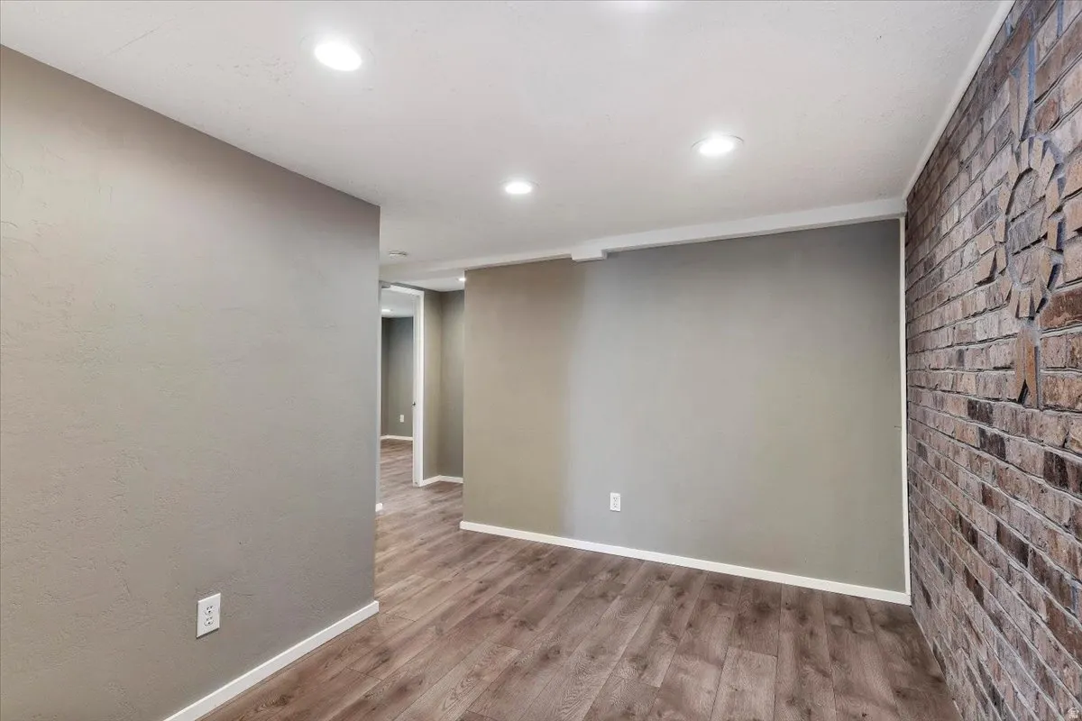 Empty room with wood finished floors, brick wall, and recessed lighting
