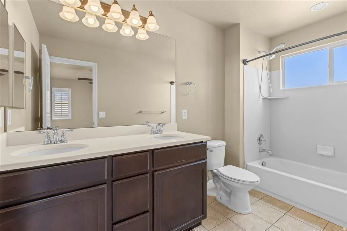 Full bathroom with double vanity, light tile patterned flooring, shower / washtub combination, and a textured ceiling