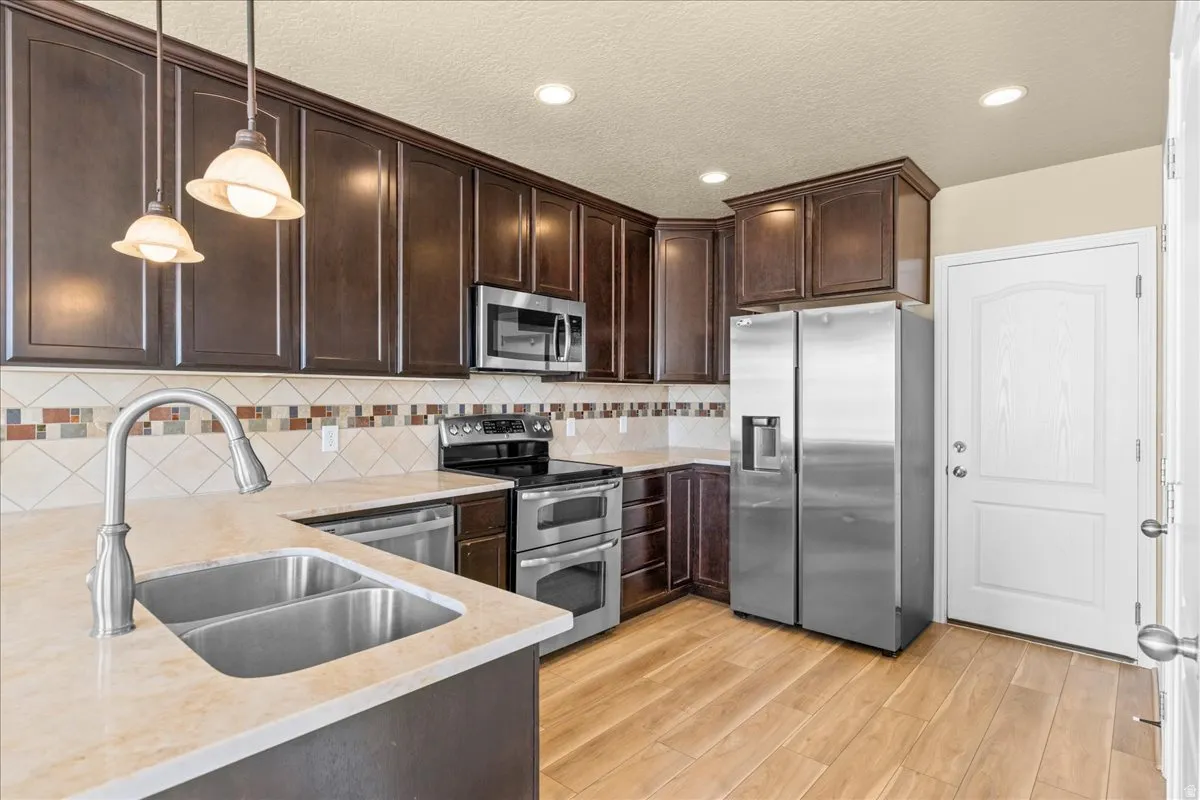 Kitchen featuring stainless steel appliances, light stone counters, dark wood finish cabinets, light wood-type flooring, and pendant lighting